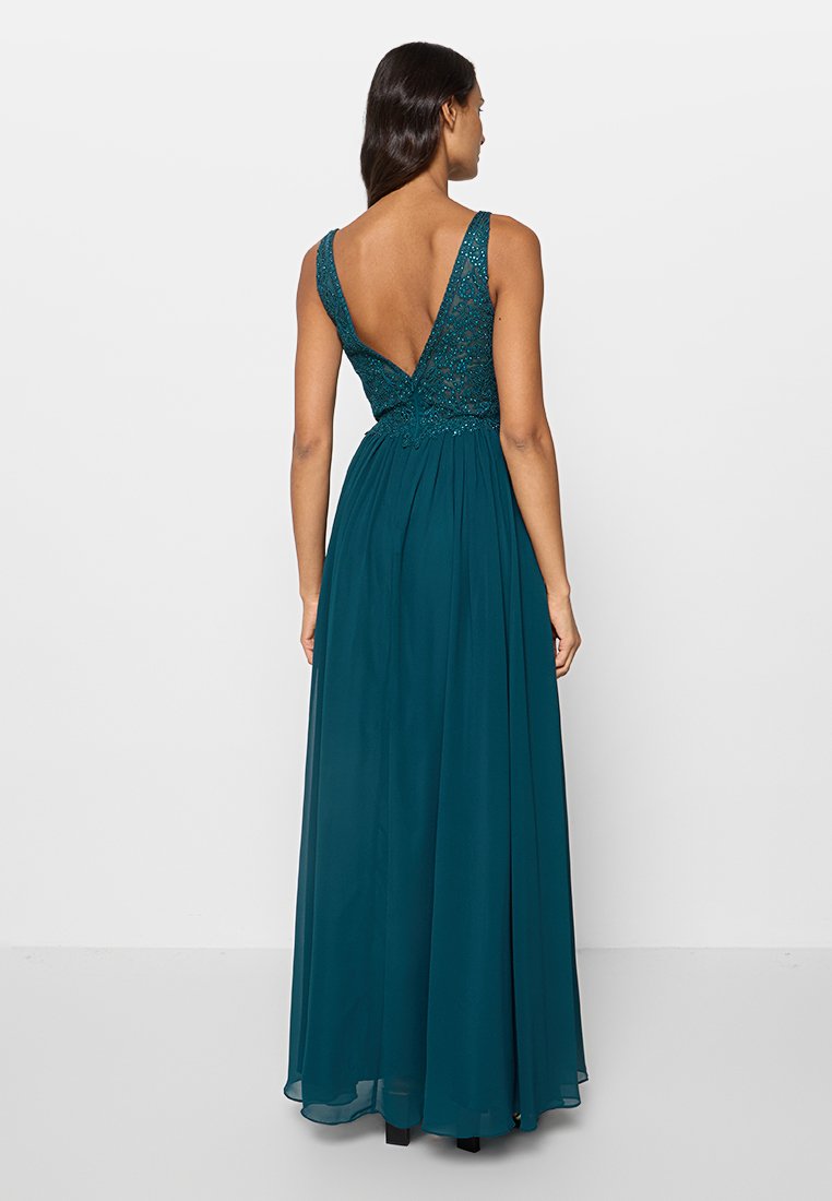 Vestido de noche en color verde azulado con un cuerpo entallado de cuentas y una falda de chiffon en línea A. Presenta un profundo escote en V en la espalda y tirantes anchos. Diseño hasta el suelo.