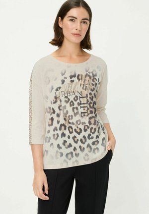 Haut en imprimé léopard beige clair, avec des manches trois-quarts et une coupe légèrement ample. Texte graphique "wild URBAN LIFE" inclus.