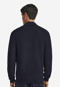 Mörkblå stickad cardigan med en texturerad mönster, långa ärmar och krage; har ribbade ärmslut och nederkant.
