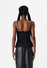 Camisón de satén negro con finas tirantes ajustables, textura suave y un dobladillo acampanado en la cintura. Sin herrajes ni patrones visibles.
