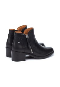 Botas de cuero negro hasta el tobillo con un tacón cuadrado de altura media, cremallera lateral y forro interior en color marrón claro. Textura suave con acentos de hardware mínimos.