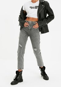 Veste de motard en cuir noir, t-shirt cropped blanc avec texte, jeans gris délavés taille haute, et bottes de combat noires à lacets avec bord en fourrure.