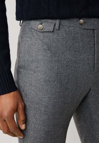 Sive vunene hlače s krojem koji prati tijelo. Imaju ravni prednji dio, dva gumba kao detalj i glatku teksturu. Prikazane su na razini struka.