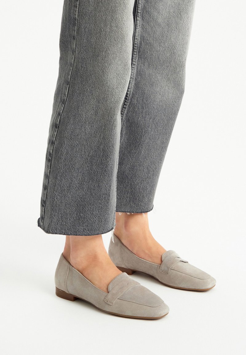Mocassini in suede grigio con tacco basso e dettaglio cucito sull'avampiede, indossati con jeans in denim grigio chiaro a pantalone corto.