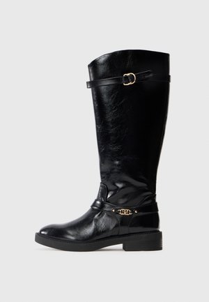 Botte noire en cuir montant jusqu'au genou avec un petit talon, boucle décorative en or près de la cheville, et une sangle avec détail de boucle en or en haut.