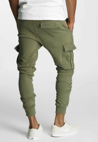 Zielone joggery cargo z tapered nogawkami, elastycznymi ściągaczami i bocznymi kieszeniami, wykonane z miękkiego, elastycznego materiału. Połączone z białymi sneakersami.