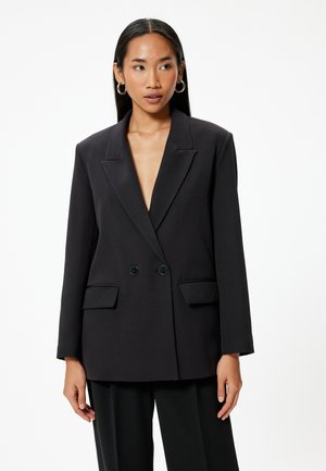 Blazer noir à double boutonnière avec un col en V profond, des épaules structurées, deux poches avant et une texture de tissu lisse.