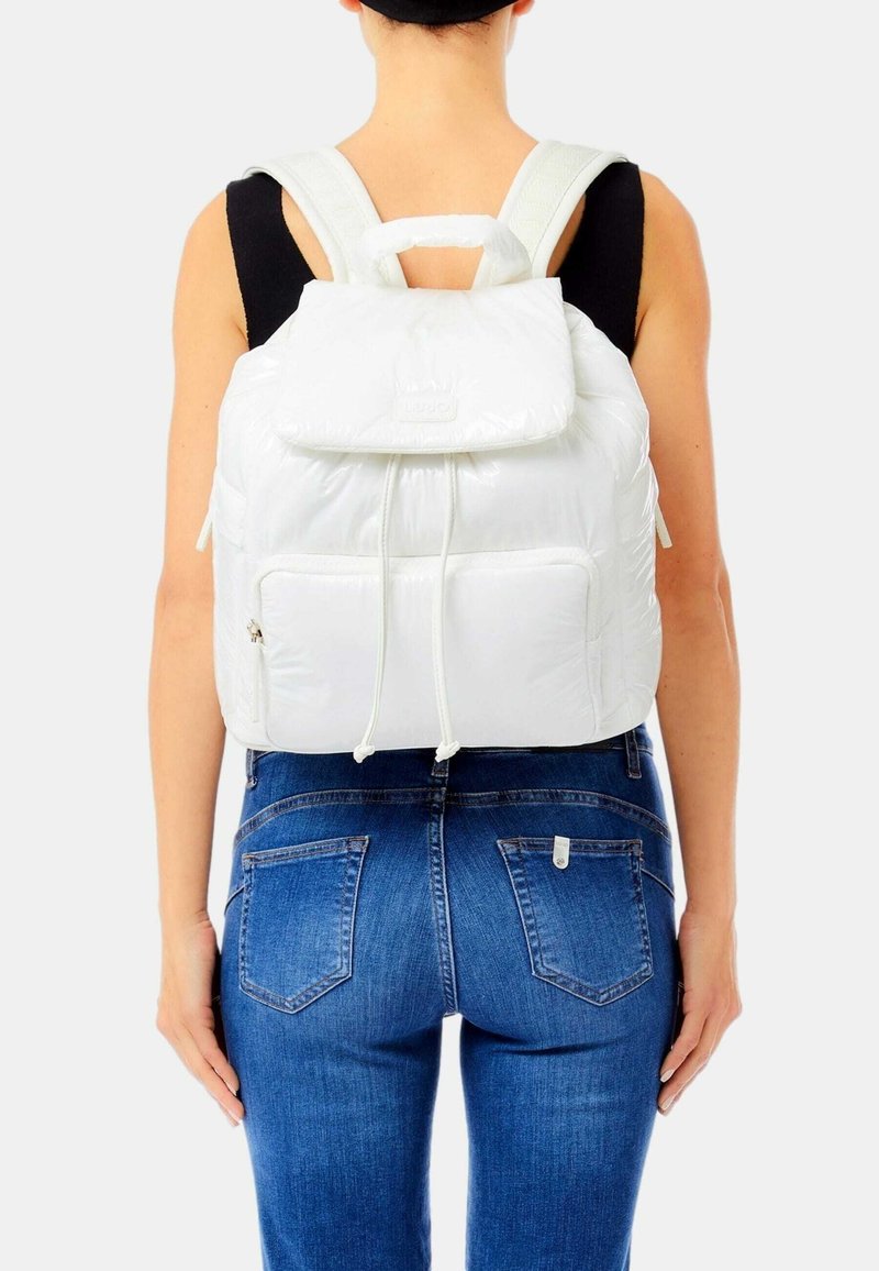 Zaino bianco in nylon con patta superiore, chiusura a cordoncino e tasca frontale. Spallacci imbottiti e maniglia superiore. Tessuto liscio e leggero.