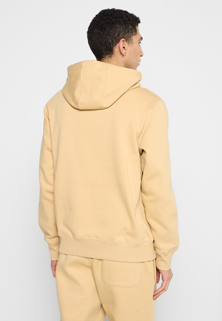 Sudadera beige con una capucha amplia y un bolsillo tipo canguro, con puños y dobladillo acanalados. Material suave con una textura lisa.