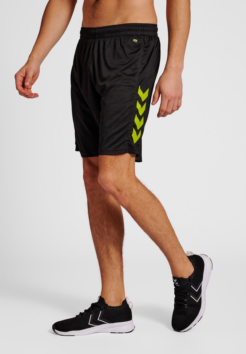 Zwarte sportshorts van een lichtgewicht materiaal, met groene chevronpatronen aan de zijkant; elastische tailleband, boven de knie lengte.