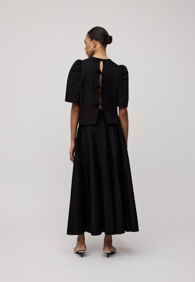 Zwarte twee-delige outfit met een cropped top met pofmouwen en een uitsnede op de rug, vastgemaakt met strikjes, gecombineerd met een vloeiende rok.