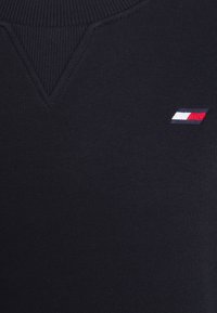 Maglione a rete blu navy con scollo a V, caratterizzato da un piccolo logo ricamato in rosso, bianco e blu sul lato sinistro. Texture morbida.