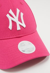 Rosa New York Yankees keps i tyg, med en vit broderad logotyp, justerbar rem och en rund etikett som anger storlek och stil.
