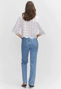 Blouse en dentelle blanche avec ourlet festonné et manches évasées, associée à un jean bleu taille haute, avec une coupe classique et des poches arrière.