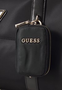 Sort nylon håndtaske med en struktureret overflade, guldhardware og en lille vedhæftet lynlåspose mærket "GUESS."