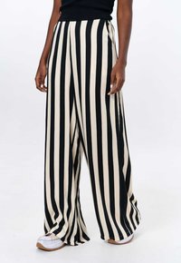 Wijdvallende broek met gedurfde zwart-witte verticale strepen, gemaakt van een soepele stof. Heeft een hoge taille en een ontspannen pasvorm.