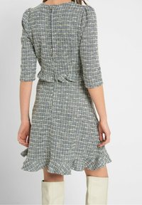 Sininen ja kerma kuvioitu mekko, jossa on kolme neljänneshihaa, muotoiltu vyötärö ja röyhelöinen helma. Näyttää olevan valmistettu teksturoidusta kankaasta, jossa on takana vetoketju.