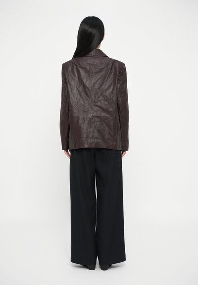 Sacou din piele burgundă închisă cu un design structurat, având guler în formă de V și mâneci lungi, asortat cu pantaloni largi negri.