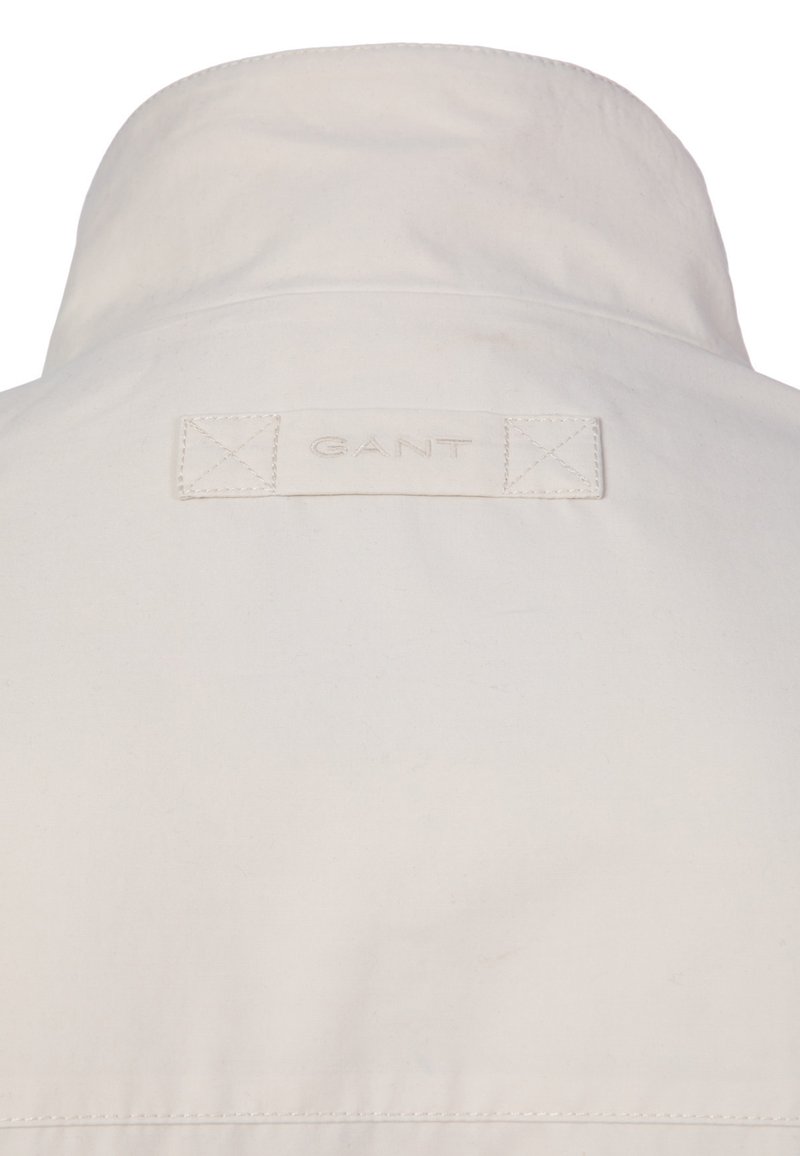 Colletto della giacca beige con etichetta di tessuto ricamata con il logo "GANT" in filo beige coordinato.