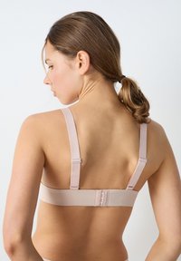 Soutien-gorge beige clair avec bretelles réglables, texture lisse et fermeture à crochets dans le dos. Design simple avec peu de détails.