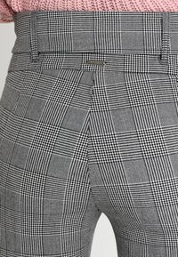 Zwart-wit houndstooth patroon broek met een getailleerde pasvorm, voorzien van een prominente tailleband en gestikte details.