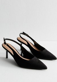 Zapatos de tacón de ante negros con punta afilada, tacones finos y parte posterior brillante. Presentan un diseño con correas y un forro interior suave.