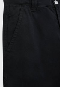 Pantalones de algodón negros con una textura suave, bolsillos estándar y cierre de botón. El diseño incluye trabillas para el cinturón y detalles de costura mínimos.