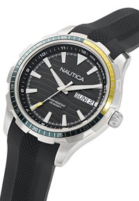 Nautica kell, millel on must tekstureeritud kellanägu, hõbedane roostevabast terasest korpus, roheline ja kollane bezel'i aktsent ning must kummist rihm. Omab kuupäeva näidikut.