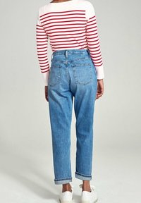 Blaue hochgeschnittene Jeans mit lockerer Passform, umgeschlagenen Säumen und Gesäßtaschen, kombiniert mit einem rot-weiß gestreiften Langarmoberteil.