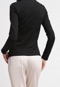 Haut à manches longues noir en tissu lisse, au design ajusté, décolleté léger, porté avec un pantalon clair, détails de couture minimalistes.