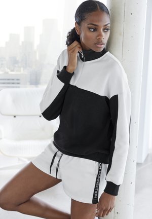 Black and white color-blocked sweatshirt with a high collar, zip detail, and ribbed cuffs. Paired with white athletic shorts featuring side branding.