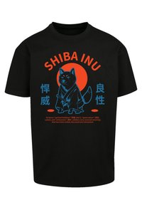 Schwarzes T-Shirt mit einem Shiba Inu Grafik in Blau und Rot. Der Text beinhaltet "SHIBA INU" und japanische Schriftzeichen, die vor einem kreisförmigen roten Hintergrund platziert sind.