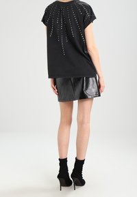 Czarna koszulka z krótkim rękawem ozdobiona kryształkami w kaskadowym wzorze na plecach, zestawiona z błyszcząca czarną mini spódnicą.