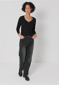 Zwarte langemouwen top met een sweetheart halslijn, gecombineerd met hoge zwarte denim jeans en stijlvolle zwarte enkellaarsjes.