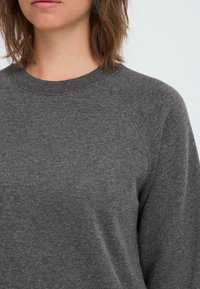Gray sweatshirt with a ribbed crew neck, raglan sleeves, and a soft texture. Fabric appears thick and comfortable.