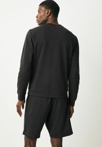 Hanorac din bumbac negru cu mâneci lungi și manșete ribbate, asortat cu pantaloni scurți care au un buzunar pe spate; design relaxat.