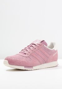 Rosa sportskor med texturerad ovandel, tre tonala ränder, vadderad krage och vit sula. Har en rundad tå och en logotyp på tungan.