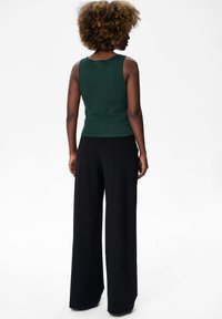 Groene geribde tanktop gecombineerd met losse zwarte wijde broek, die een aansluitende silhouet en textuur stof laat zien. Eenvoudig ontwerp van de halslijn.