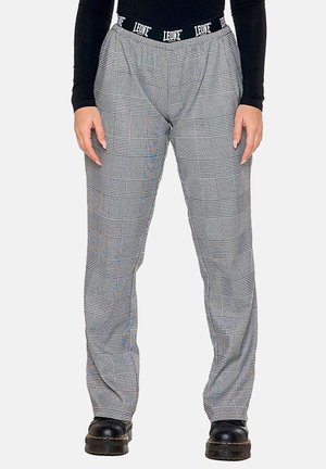 Person wearing black boots, gray plaid pants, and a black long-sleeve top with visible "LEONE" waistband details.