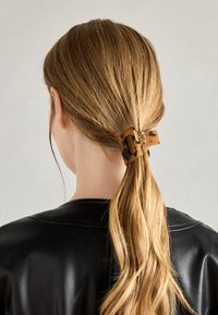 Tortoiseshell hair clip fastening a ponytail, made of glossy plastic. The design features a rectangular shape with an open grid pattern.