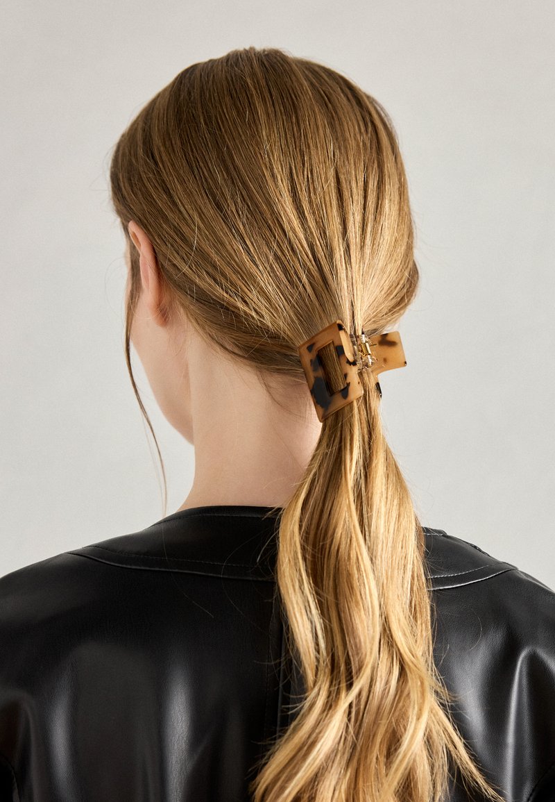 Tortoiseshell hair clip fastening a ponytail, made of glossy plastic. The design features a rectangular shape with an open grid pattern.