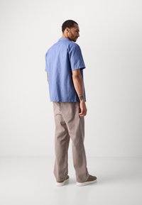 Camicia azzurra chiara a maniche corte realizzata in tessuto morbido, abbinata a pantaloni beige chiaro. L'outfit presenta una vestibilità rilassata e una silhouette semplice.