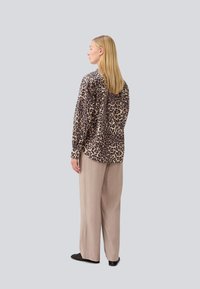 Camicia con stampa leopardata, maniche lunghe, vestibilità morbida, tessuto leggero e dettagli con bottoni, abbinata a pantaloni beige chiaro a gamba larga.