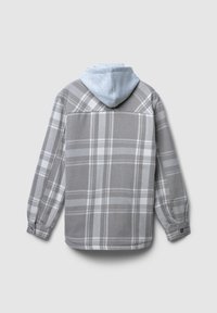 Szara marynarka w kratę z jasnoniebieską bluzą z kapturem. Posiada zapięcia na guziki przy mankietach oraz gładką teksturę materiału. Na plecach widnieją wyraźne wzory w kratę.