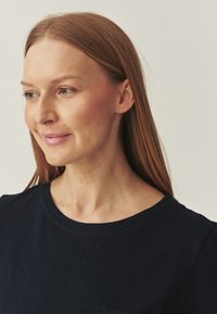 Sötétkék, kereknyakú póló, puha, texturált anyagból készült, melyen egy kis mellsz zseb és rövid ujj található. Minimális dizájn részletek.