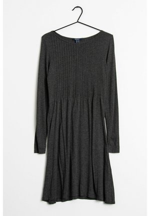 Mørkegrå langærmet strikket kjole hængende på en sort bøjle, med lodrette plisseringer på den øverste halvdel og en udvidet nederdel.