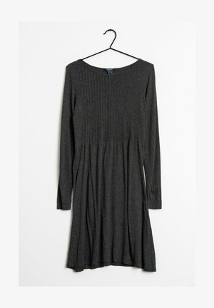 Mørkegrå langærmet strikket kjole hængende på en sort bøjle, med lodrette plisseringer på den øverste halvdel og en udvidet nederdel.