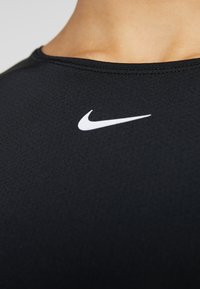 Camiseta deportiva negra con cuello redondo y un pequeño logo blanco de Nike en la zona del pecho, fabricada con un tejido suave y elástico.