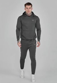 Felpa con cappuccio grigio scuro e pantaloni jogger abbinati in tessuto liscio. Presenta una tasca frontale, polsini a costine e un marchio minimale sul petto.
