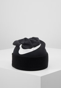 Zwart gebreide beanie met een omgevouwen manchet, voorzien van een opvallend wit Nike-logo aan de voorkant. Zachte textuur, ronde vorm.